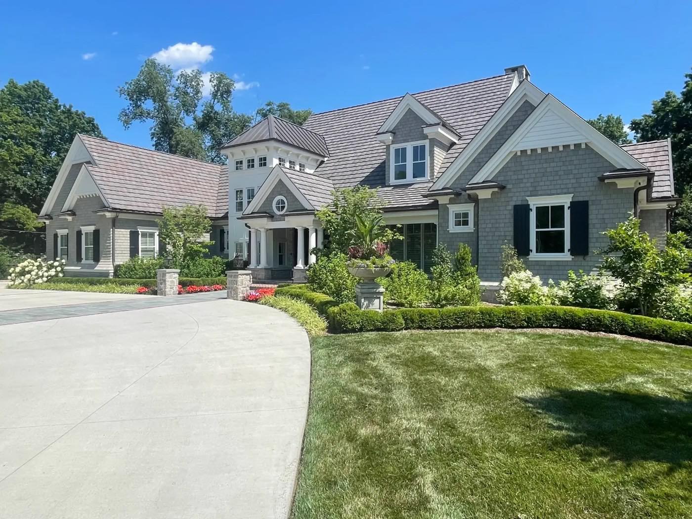 A green lawn beside a curved driveway, with boxwood hedges and hydrangeas in front of a shingle-style home