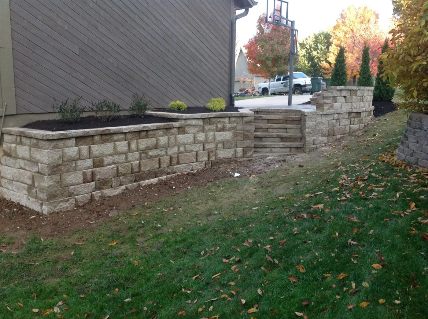 Block retaining wall with built-in steps and new plantings, with a Strahm Lawns truck in the driveway